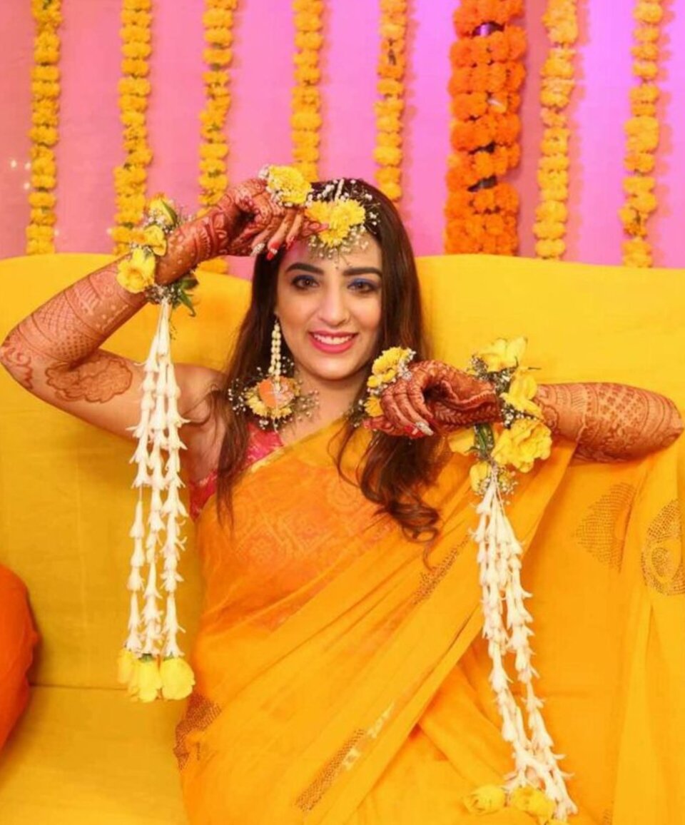 Bride wearing floral jewellery at haldi ceremony with marigold backdrop
